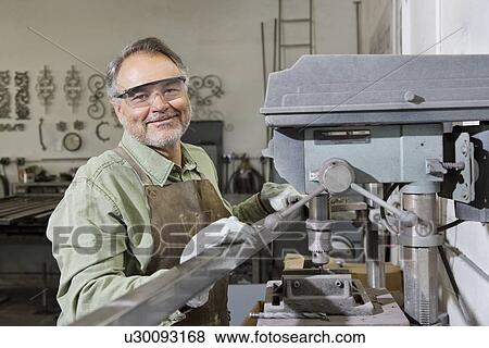 Portrait of a happy mature man wearing protective eyewear standing by machinery in workshop View Large Photo Image Stock Photo - Portrait of a happy mature man wearing protective eyewear standing by machinery in workshop. Fotosearch