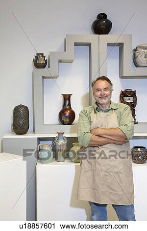 Stock Image - Portrait of a happy mature potter with arms crossed standing in pottery workshop. Fotosearch