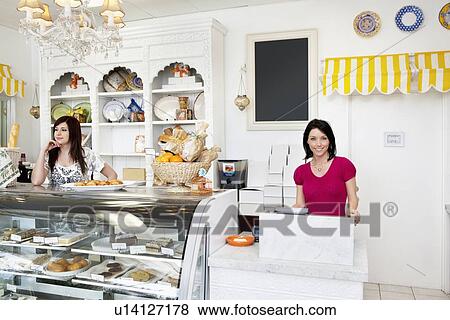 Stock Photo - Portrait of a happy mid adult woman standing at checkout counter with coworker in cake shop. Fotosearch