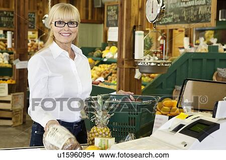 Portrait of a happy senior female with shopping basket standing by cash register in grocery store View Large Photo Image Picture - Portrait of a happy senior female with shopping basket standing by cash register in grocery store. Fotosearch