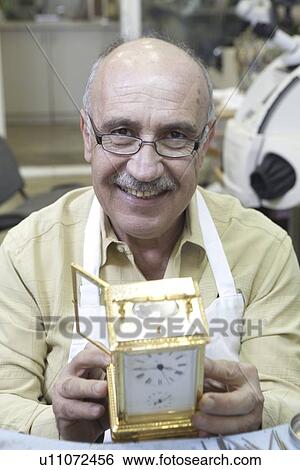Stock Photograph - Portrait of a happy skilled worker with clock in repair shop. Fotosearch