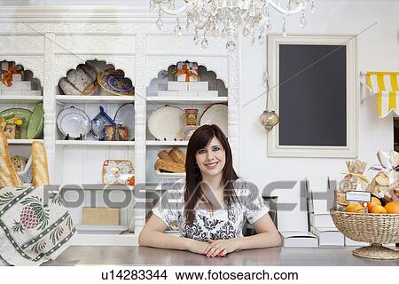 Picture - Portrait of a happy young caterer at counter in cake shop. Fotosearch