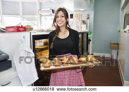 Stock Photo - Portrait of a happy young female carrying tray in bakery. Fotosearch