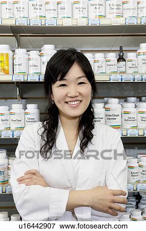 Stock Photo - Portrait of a happy young female with arms crossed in drugstore. Fotosearch