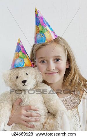 Stock Photo - Portrait of a happy young girl wearing party hat with soft toy over colored background. Fotosearch