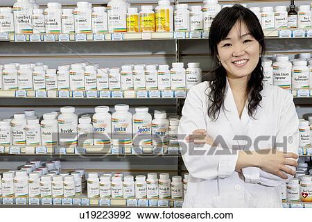 Stock Image - Portrait of a happy young woman with arms crossed in drugstore. Fotosearch