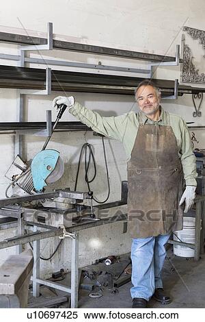 Stock Photography - Portrait of a mature man standing by electric saw in workshop. Fotosearch