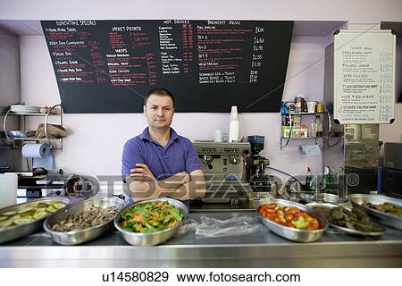Stock Photo - Portrait of a mid adult man standing with arms crossed in cafe. Fotosearch