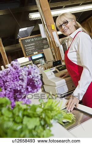 Stock Image - Portrait of a senior employee at checkout counter in market. Fotosearch