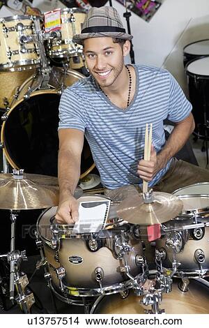 Picture - Portrait of a young customer with drum set in music store. Fotosearch