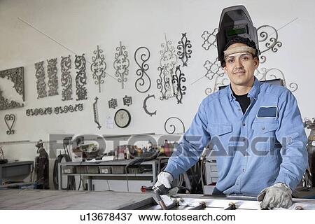 Stock Photo - Portrait of a young male worker wearing protective gear in metal workshop. Fotosearch