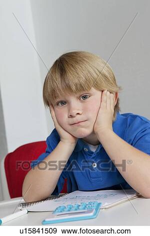 Portrait of bored boy sitting at table with book and calculator View Large Photo Image Stock Photo - Portrait of bored boy sitting at table with book and calculator. Fotosearch