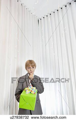 Stock Image - Portrait of boy with hand on chin giving gift. Fotosearch