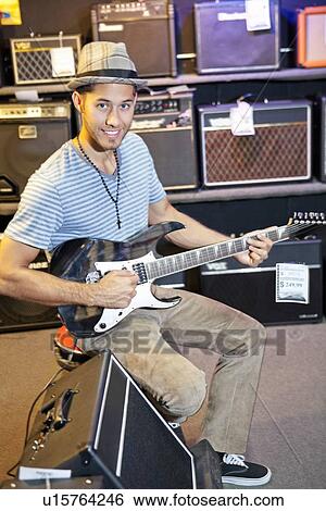 Stock Photograph - Portrait of happy customer playing electric guitar in music store. Fotosearch