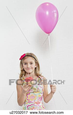 Portrait of happy girl holding cupcake and party balloon over colored background View Large Photo Image Stock Photo - Portrait of happy girl holding cupcake and party balloon over colored background. Fotosearch