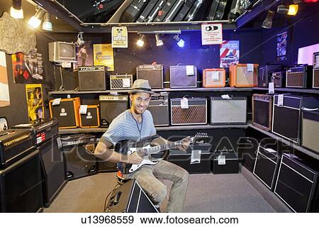 Stock Photo - Portrait of happy young male customer strumming the guitar in music store. Fotosearch