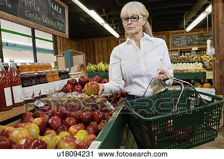 Stock Image - Senior woman shopping for apples in market. Fotosearch