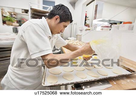 Stock Photo - Side view of a young male baker making pastry in bakery. Fotosearch