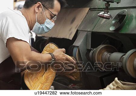 Stock Image - Side view of mature shoemaker rubbing sole in machinery. Fotosearch