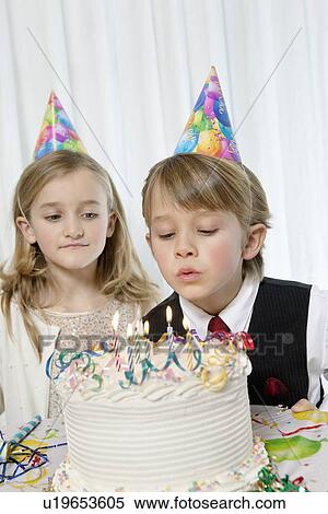 Stock Photography - Sister watching while birthday boy blowing candles on cake. Fotosearch
