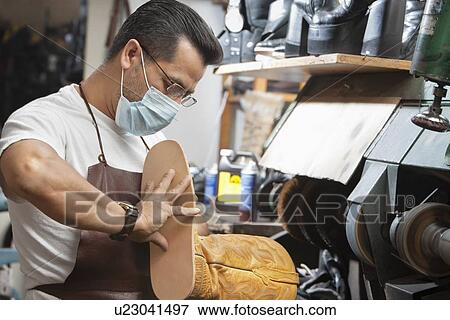 Stock Photo - Skilled cobbler wearing mask working on shoe sole in workshop. Fotosearch