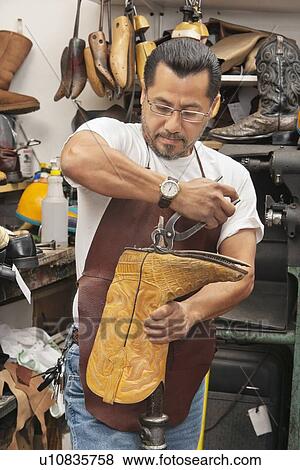 Stock Photo - Skilled shoemaker cutting boot's sole in workshop. Fotosearch
