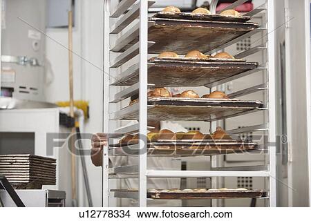 Picture - Young baker pushing bread cart in bakery. Fotosearch