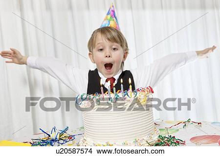 Young birthday wearing party hat with arms outstretched blowing candles on cake View Large Photo Image Picture - Young birthday wearing party hat with arms outstretched blowing candles on cake. Fotosearch