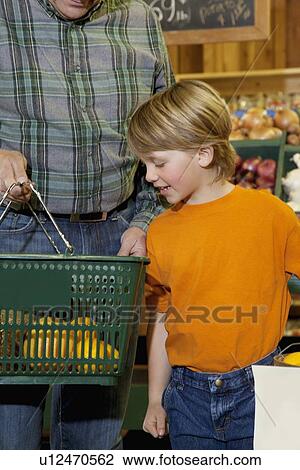 Stock Image - Young boy looking at shopping basket with grandfather in market. Fotosearch