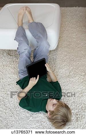 Young boy lying on rug with tablet pc View Large Photo Image Stock Image - Young boy lying on rug with tablet pc. Fotosearch