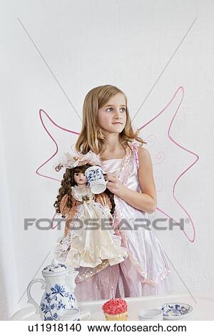 Young girl standing with doll and cup over colored background View Large Photo Image Stock Image - Young girl standing with doll and cup over colored background. Fotosearch