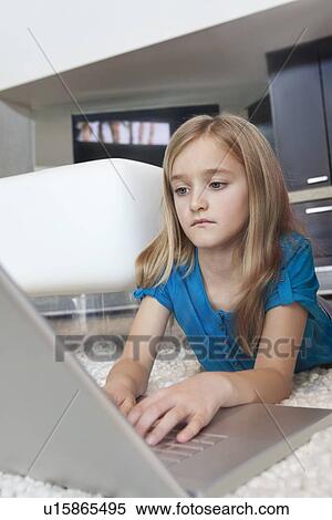 Young girl using laptop while lying on rug in house View Large Photo Image Stock Photography - Young girl using laptop while lying on rug in house. Fotosearch