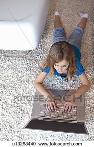 Stock Image - Young girl with laptop lying on rug. Fotosearch