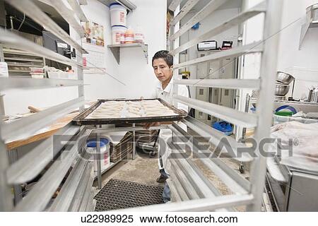 Young male baker placing bread tray on cart in commercial kitchen View Large Photo Image Stock Photography - Young male baker placing bread tray on cart in commercial kitchen. Fotosearch
