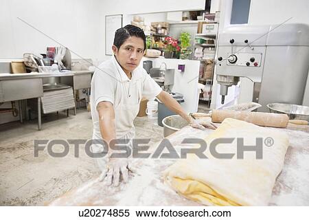 Stock Photography - Young male baker standing near yellow dough in bakery kitchen. Fotosearch