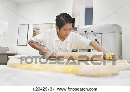 Stock Photo - Young male baker working with rolling pin on yellow dough in bakery. Fotosearch