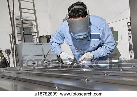 Young male worker wearing protective gear welding in workshop View Large Photo Image Stock Photo - Young male worker wearing protective gear welding in workshop. Fotosearch