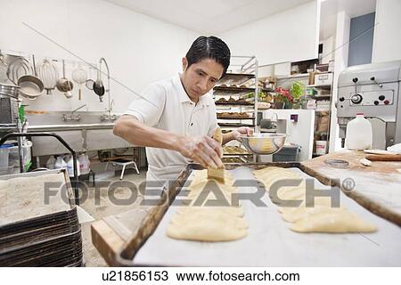 Stock Image - Young man preparing dough in bakery kitchen. Fotosearch