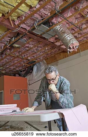 Architect concentrating on building plans at construction site View Large Photo Image Stock Photo - Architect concentrating on building plans at construction site. Fotosearch