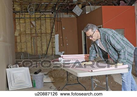Architect looking at building plans at construction area View Large Photo Image Stock Photograph - Architect looking at building plans at construction area. Fotosearch