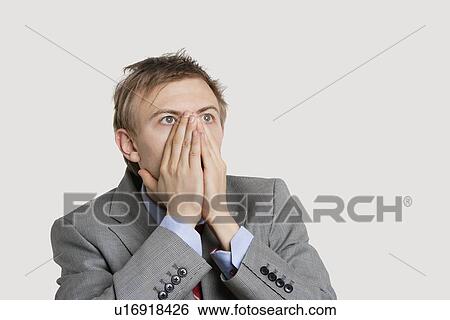 Close-up of a shocked businessman with hands covering mouth over light gray background View Large Photo Image Stock Photograph - Close-up of a shocked businessman with hands covering mouth over light gray background. Fotosearch