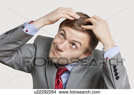Picture - Close-up of confused businessman touching head with funny face over colored background. Fotosearch