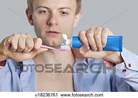 Stock Image - Close-up of young male removing toothpaste on brush over colored background. Fotosearch