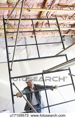 Stock Image - Construction worker looking up at incomplete ceiling. Fotosearch
