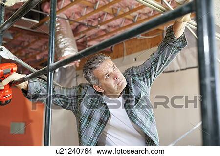 Picture - Contractor looking up while standing near scaffolding. Fotosearch