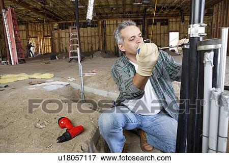 Stock Photo - Contractor working with screwdriver on pipe. Fotosearch