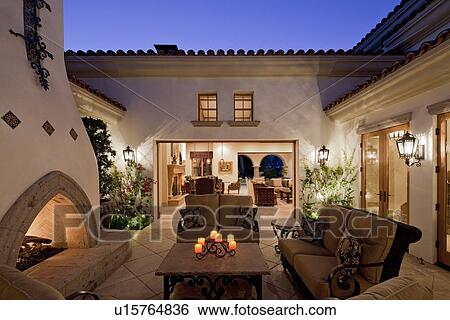 Stock Photograph - Fireplace with seating furniture in courtyard of luxury mansion in night. Fotosearch