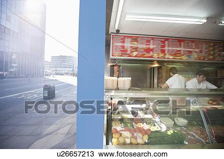 Stock Image - Food in display case with men working in shop. Fotosearch