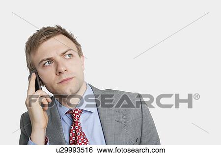 Handsome young businessman looking away while listening carefully to cell phone over colored background View Large Photo Image Stock Photograph - Handsome young businessman looking away while listening carefully to cell phone over colored background. Fotosearch