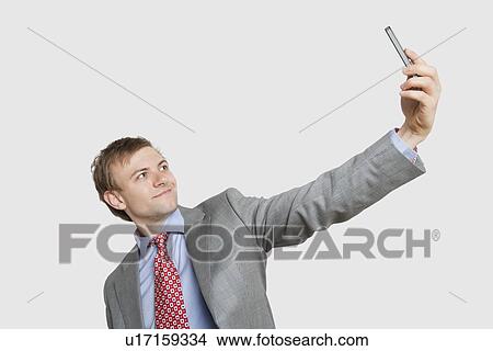 Picture - Handsome young businessman taking self-portrait photograph over colored background. Fotosearch